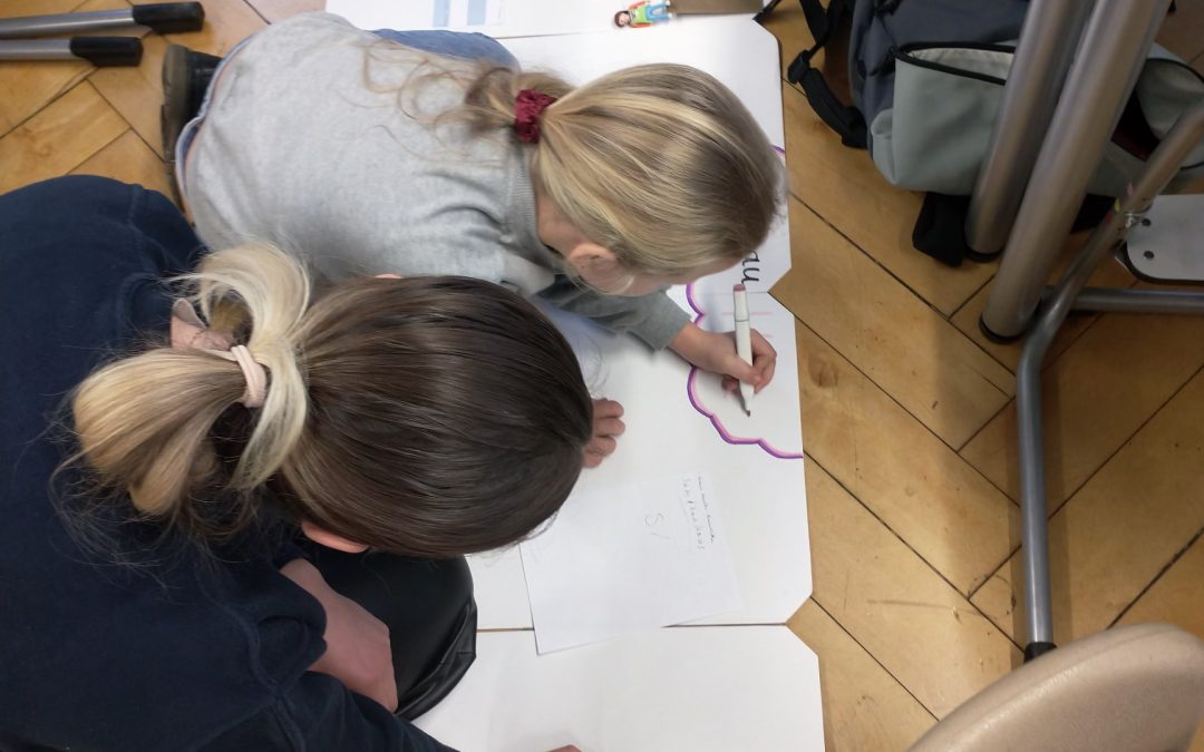 Studierende und Kinder arbeiten gemeinsam auf dem Boden an einem Konzept für ein Erklärvideo